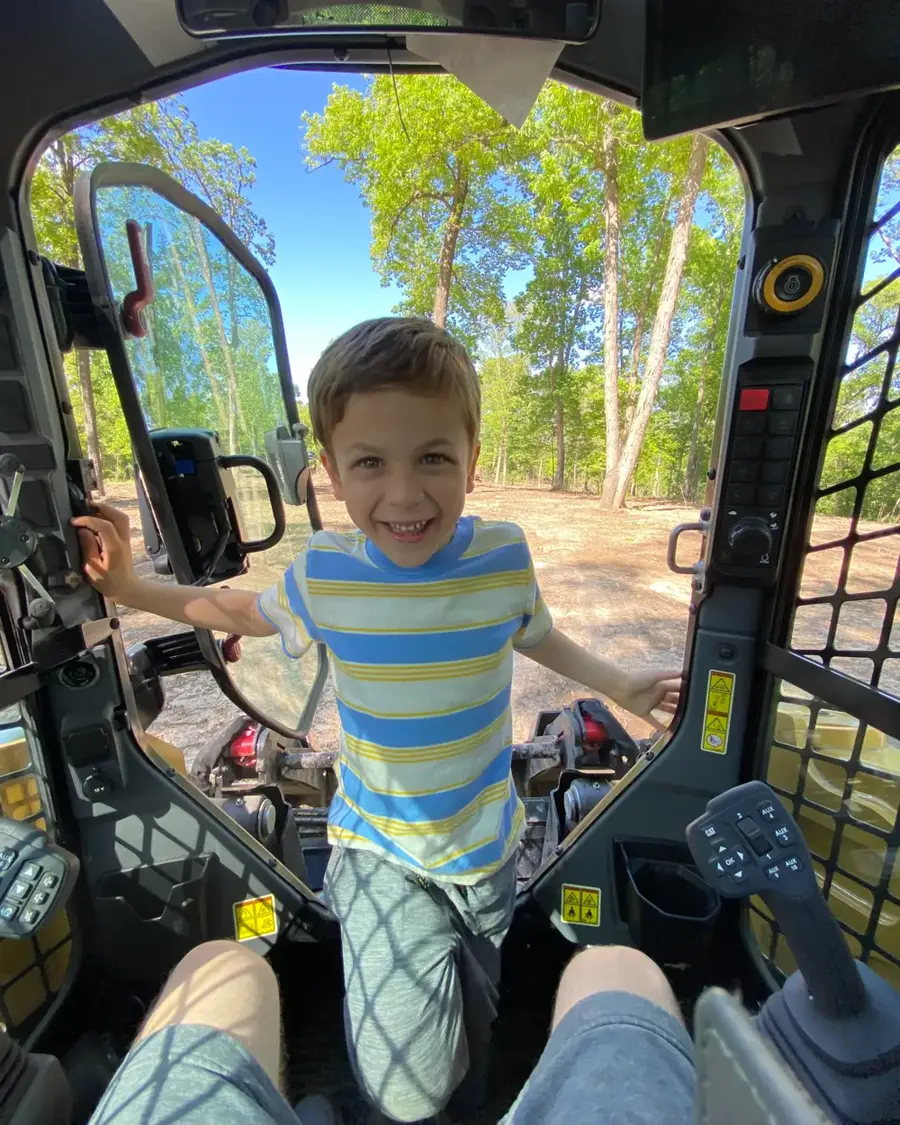Matt's son standing in the cab of a track loader on a wooded Wicks job site